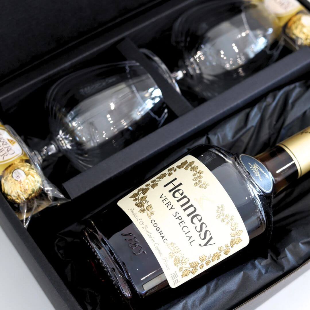 Hennessy cognac bottle with two glasses and Ferrero Rocher chocolates in a black gift box.