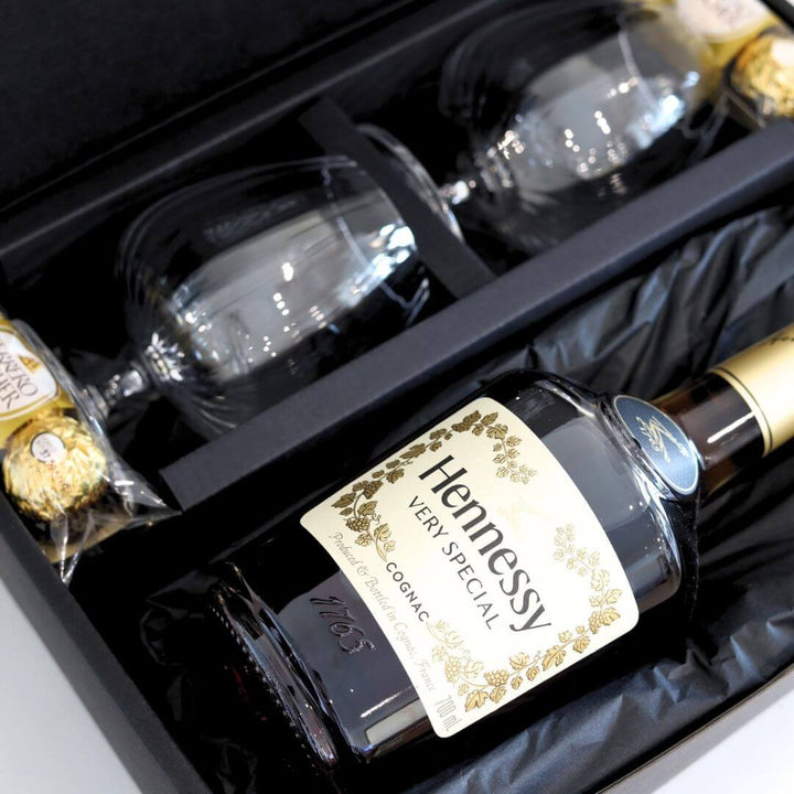 Hennessy cognac bottle with two glasses and Ferrero Rocher chocolates in a black gift box.